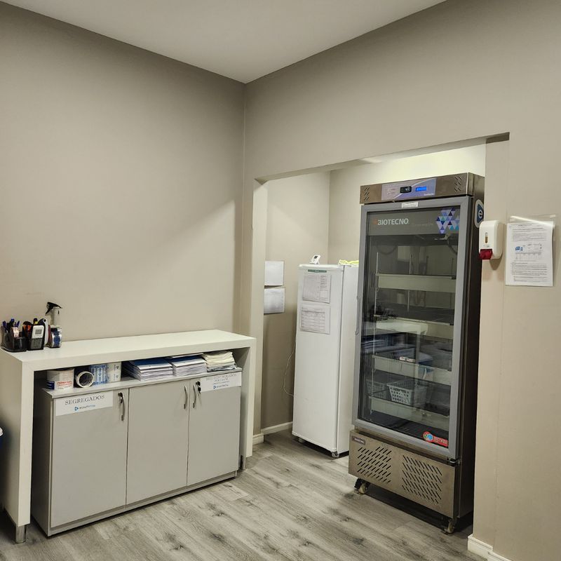 Sala de armazenamento com refrigerador vertical para medicamentos e armário identificado como refrigerados.